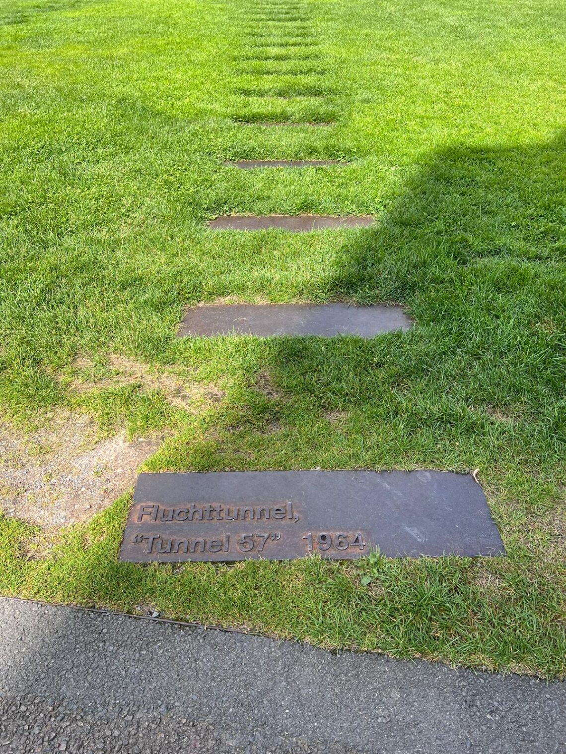 laca de pedra no chão com a inscrição "Fluchttunnel, 'Tunnel 57' 1964" em um gramado verde.